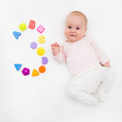 Portrait of a sweet infant baby girl wearing a red dress and bonnet, isolated on white in studio with number tree from toys, cubes, letters and molds