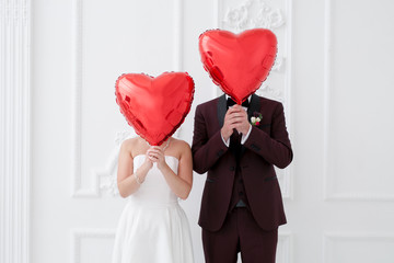Two newlyweds cover their faces with heart-shaped balloons