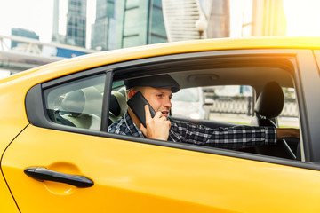 Photo of young man talking on phone sitting in back seat of taxi on summer day.