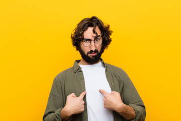 young crazy man pointing to self with a confused and quizzical look, shocked and surprised to be...