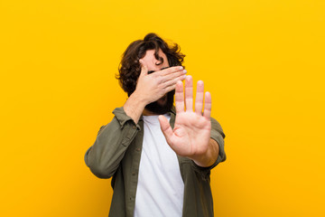 young crazy man covering face with hand and putting other hand up front to stop camera, refusing...