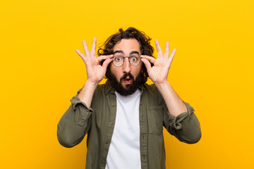 young crazy man feeling shocked, amazed and surprised, holding glasses with astonished,...