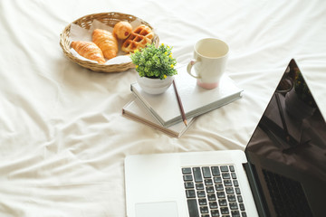Book, pencil, notebook, bread, coffee and laptop on the bed In the morning.