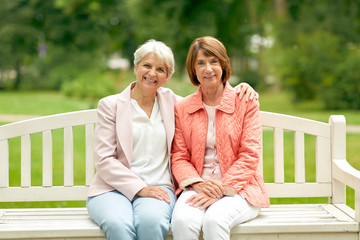 old age, retirement and people concept - two senior women or friends sitting on bench at summer park
