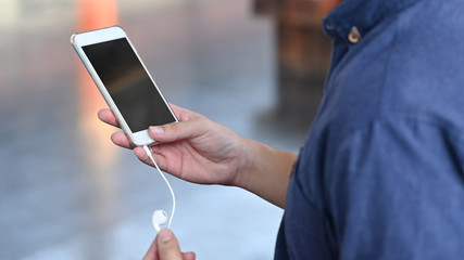 Closeup man holding mobile phone and ear phone on train station.