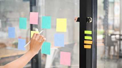 Businesswoman reading sticky notes on glass wall with her working.