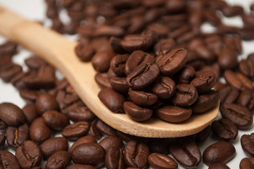 Closeup of coffee beans in a wooden spoon on white background