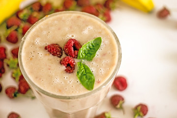 Appetizing milkshake with raspberries Delicious creamy cocktail with fresh berries and banana on blurred white background. Raspberry smoothie with banana and coconut milk. The concept of healthy diet