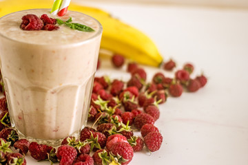 Appetizing milkshake with raspberries Delicious creamy cocktail with fresh berries and banana on blurred white background. Raspberry smoothie with banana and coconut milk. The concept of healthy diet
