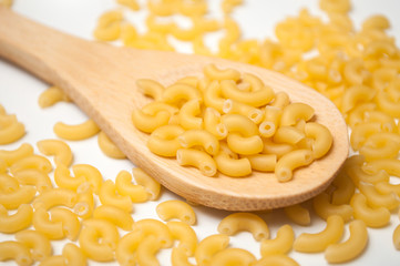 Closeup of raw pasta in a wooden spoon on white background