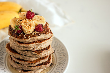 Delicious banana pancakes on white plate. Stack of homemade appetizing fritters with sliced banana served on blurred white background.