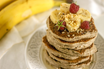 Delicious banana pancakes on white plate. Stack of homemade appetizing fritters with sliced banana served on blurred white background. Coconut Gluten Free Baking.  Homemade breakfast with pancakes