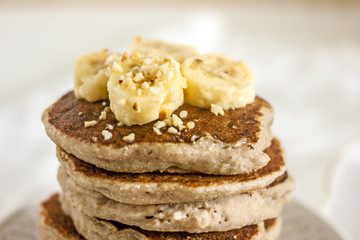 Delicious banana pancakes on white plate. Stack of homemade appetizing fritters with sliced banana served on blurred white background. Coconut Gluten Free Baking.  