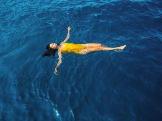 young woman in a one-piece yellow swimsuit floats on the surface of the water.