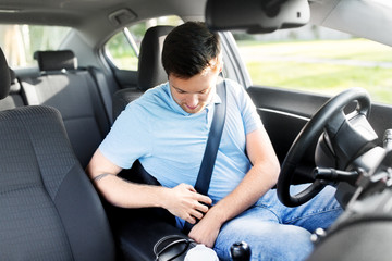 transport, vehicle and safe driving concept - man or car driver fastening safety seat belt in summer