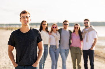 friendship, leisure and people concept - happy man in glasses with group of friends on beach in summer