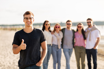 Obraz premium friendship, leisure and people concept - happy man with group of friends on beach in summer showing thumbs up
