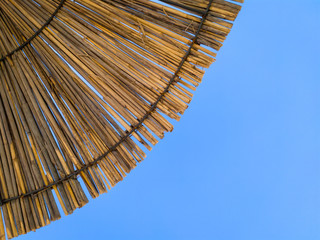 Canopy of a beach sunshade made of reed. Cone of a straw parasol against clear blue sky. Upward view.  © Predrag Jankovic