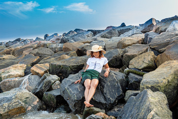 Lady relaxing on boulders by the beach under a blue sky