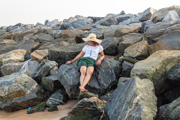 Young African lady laying on a pile of boulders by the beach