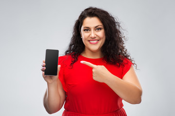 Naklejka premium people and portrait concept - happy woman in red dress showing smartphone with blank screen over grey background