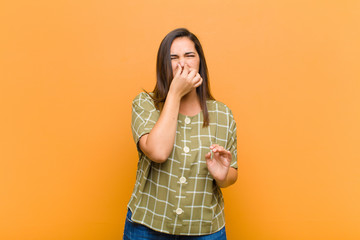 young pretty woman feeling disgusted, holding nose to avoid smelling a foul and unpleasant stench...