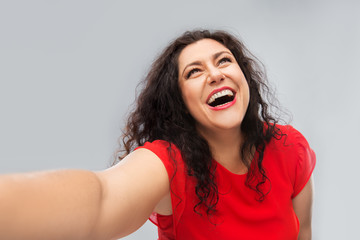 people and portrait concept - happy woman in red dress taking selfie over grey background