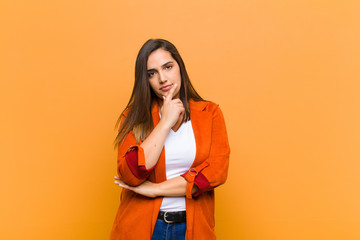 young pretty woman looking serious, thoughtful and distrustful, with one arm crossed and hand on...