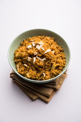Wheat Laapsi/Lapsi/Shira/Halwa is an Indian sweet dish made of broken wheat or Daliya pieces and ghee along with nuts, raisins and dried fruits. It's a healthy food. served in a bowl, selective focus