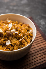 Wheat Laapsi/Lapsi/Shira/Halwa is an Indian sweet dish made of broken wheat or Daliya pieces and ghee along with nuts, raisins and dried fruits. It's a healthy food. served in a bowl, selective focus