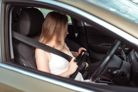 girl car's interior calls on phone, looks in rearview mirror, parks parking lot of shopping center, holds it fastened by steering wheel. Woman in summer sunglasses in city wearing a pink dress.