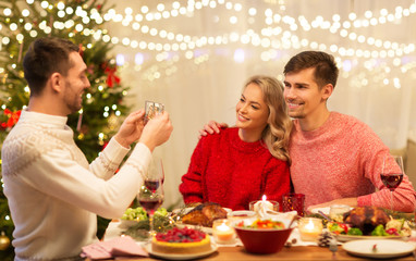 holidays and celebration concept - happy man photographing his friends at christmas dinner