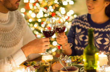 holidays, family and celebration concept - close up of happy couple having christmas dinner, drinking red wine and clinking glasses