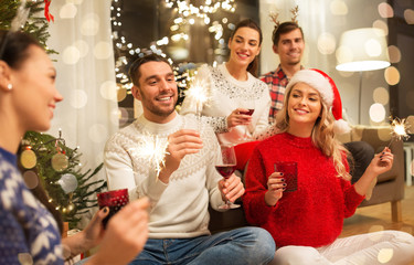 celebration and holidays concept - happy friends with glasses and sparklers celebrating christmas at home party and drinking red wine
