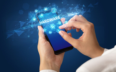Female hand holding smartphone with HARDWARE inscription, modern technology concept