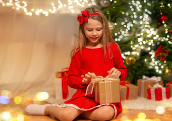 Fototapeta na wymiar christmas, holidays and childhood concept - smiling girl in red dress with gift box at home