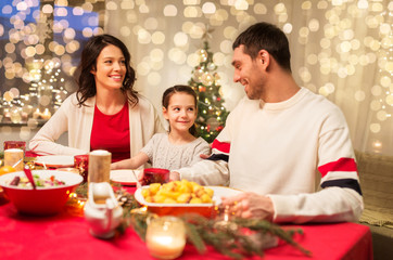 holidays, family and celebration concept - happy mother, father and little daughter having christmas dinner at home