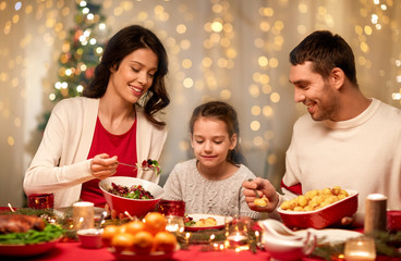 holidays, family and celebration concept - happy mother, father and little daughter having christmas dinner at home