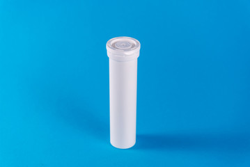 Round white tube with a lid for effervescent tablets, vitamins. New tube with the drug isolated on a blue background. copy space. The concept of health, the treatment of viral diseases and headache