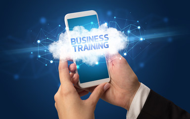 Female hand touching smartphone with BUSINESS TRAINING inscription, cloud business concept