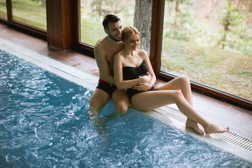 Cheerful youthful guy and lady resting by swimming pool in spa