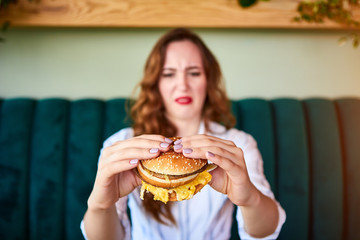 Pretty woman is refusing to eat unhealthy hamburger. She is looking at it with disgust