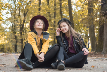 Beautiful young girl resting on street. Emotional conversation sisters. Teenage girls rest and talk for a walk in the autumn park. Young students communicate in nature.