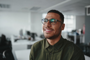 Portrait of a thoughtful smiling young modern business man at office looking away