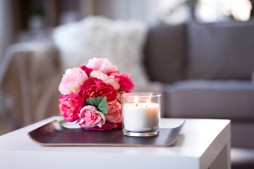 decoration, hygge and cosiness concept - burning fragrance candle and flower bunch at cozy home