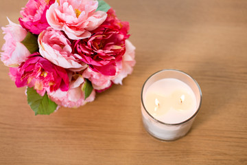 Obraz na płótnie Canvas decoration, hygge and cosiness concept - burning fragrance candle and flower bunch on wooden table