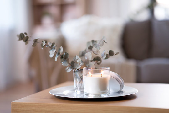 Decoration, Hygge And Cosiness Concept - Burning White Fragrance Candle On Tray And Branches Of Eucalyptus Populus On Table At Cozy Home