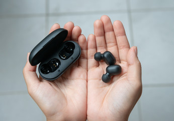 Close up of woman is holding the black true wireless earbuds case in hand - obrazy, fototapety, plakaty