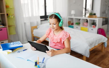 children, education and technology concept - happy student girl in headphones with tablet computer at home desk