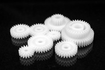 Several white plastic gears on a black mirror background. Mechanical repair. Fix. Reflection. Repair shop. Cogwheels. Elements of a large mechanism. Harmonious work. 